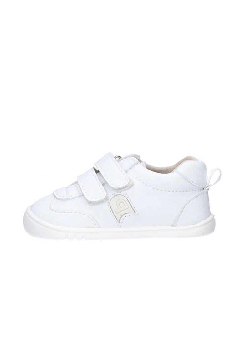 Zapatilla blanca para niño pequeño con dos tiras de velcro, suela de goma y un pequeño lazo en el talón para facilitar el calzado.