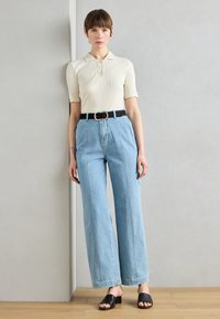 Polo shirt bianco a coste con maniche corte, pantaloni a vita alta in denim azzurro chiaro a gamba larga e una cintura nera. Sandali con tacco aperti neri.