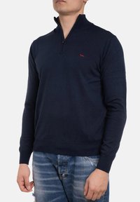 Maglione navy con colletto con zip, realizzato in un morbido tessuto a maglia. Presenta un piccolo logo rosso sul petto e polsini e orlo a coste.