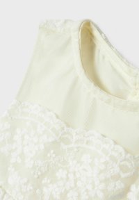Lichtgele kleding met witte bloemenkantaccenten, zachte textuur, mouwloos ontwerp en ronde halslijn. Subtiele glans in de stof.
