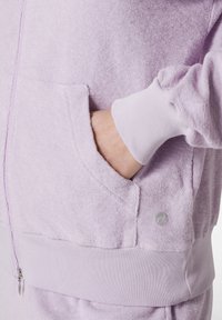 Felpa con zip color lilla realizzata in morbido terrycloth, con tasca frontale e polsini a costine, dotata di un piccolo logo sul lato inferiore.