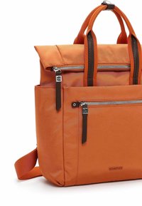 Zaino arancione realizzato in tessuto resistente, con molteplici tasche con cerniera, dettagli in pelle marrone e un design strutturato con doppi manici.