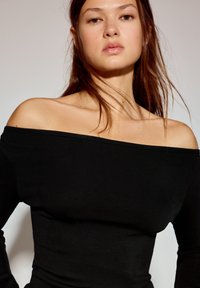 Czarny top odsłaniający ramiona, wykonany z prążkowanego materiału, z długimi rękawami i dopasowanym krojem. Gładka faktura z szerokim dekoltem.