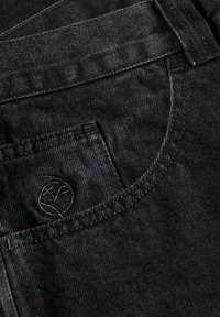 Jeans de mezclilla negros con un tejido texturizado, bolsillos cosidos y un logo sutil en el bolsillo trasero. El diseño es simple y clásico.