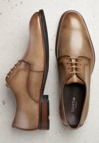Bruine leren dresschoenen hebben een gladde textuur, veters, een ronde neus en een contrasterende donkere zool met een houten accent bij de hak.