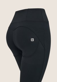 Mustat leggingsit, jotka on valmistettu joustavasta kankaasta, joissa on korkea vyötärö, kaareva sauman yksityiskohta ja pieni hopea logo takataskussa.