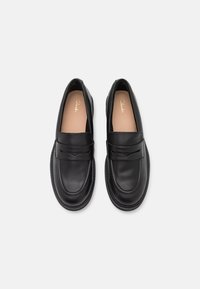 Mocassins en cuir noir avec une finition lisse, dotés d'une sangle à l'avant et d'un bout rond. Les semelles intérieures sont beiges avec un logo en relief.