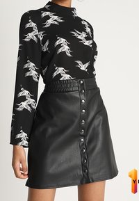 Svart långärmad topp med vita fågelmönster och en svart fusk läderkjol med knäppning fram och elastisk midja.