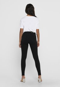 Jean skinny de talle alto en negro con diseño de cinco bolsillos. Combinados con una camiseta blanca y sandalias de tacón transparente. Textura suave, ajuste elegante.