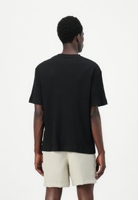 T-shirt noir à rayures avec des manches courtes et un col rond, associé à un short beige clair. Le tissu a une apparence texturée et une coupe décontractée.