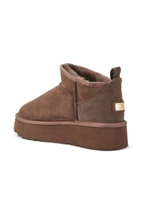 Botas de tobillo de ante marrón con una suela de plataforma gruesa, forro interior suave, detalles de costura y un pequeño acento metálico de marca en el talón.