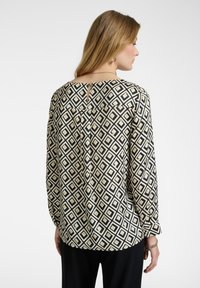 Långärmad blus i svart, kräm- och guld geometriskt mönster. Har en rundad halsringning och en nyckelhålsdetalj bak.