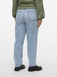 Heledsinised teksapüksid lõdva istuvusega, vertikaalsete tagataskutega ja kergelt tuhmse tekstuuriga, millega on kombineeritud mustad mokassiinid.