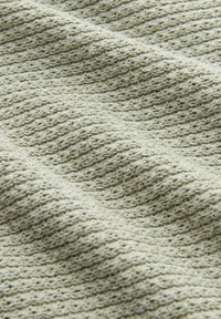 Tissu tricoté gris clair avec un motif texturé en forme de gaufre et des plis de surface doux et irréguliers.