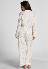 Witte pyjama set met kleine bloemmotieven in zwart en rood. Los vallende top met lange mouwen en rechte pijpen. Zachte stofdikte.