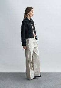 Zwarte cropped jas van suède over een lichtroze blouse, gecombineerd met crème wijde broek met strepen en zwarte schoenen. Eenvoudig, strak ontwerp.