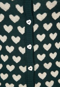 Ciemnozielony dzianinowy materiał z powtarzającym się wzorem kremowych serc i białych guzików w kształcie serca wzdłuż centralnego szwu.