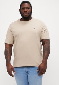 Beige bomull t-skjorte med rund hals og korte ermer, med en liten logo på venstre bryst, båret med lyseblå denimjeans.