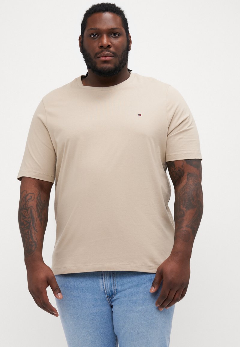 Beige bomull t-skjorte med rund hals og korte ermer, med en liten logo på venstre bryst, båret med lyseblå denimjeans.