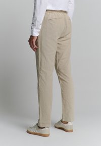 Lichtbeige broek met een ontspannen pasvorm, voorzien van een elastische tailleband en subtiele textuur, in combinatie met lichtgekleurde sneakers.