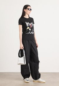 Mustaga graafikaga T-särk, mustad laiad püksid, hõbedased spordijalatsid ja metallik hõbedane käsikott kõverate käepidemetega.