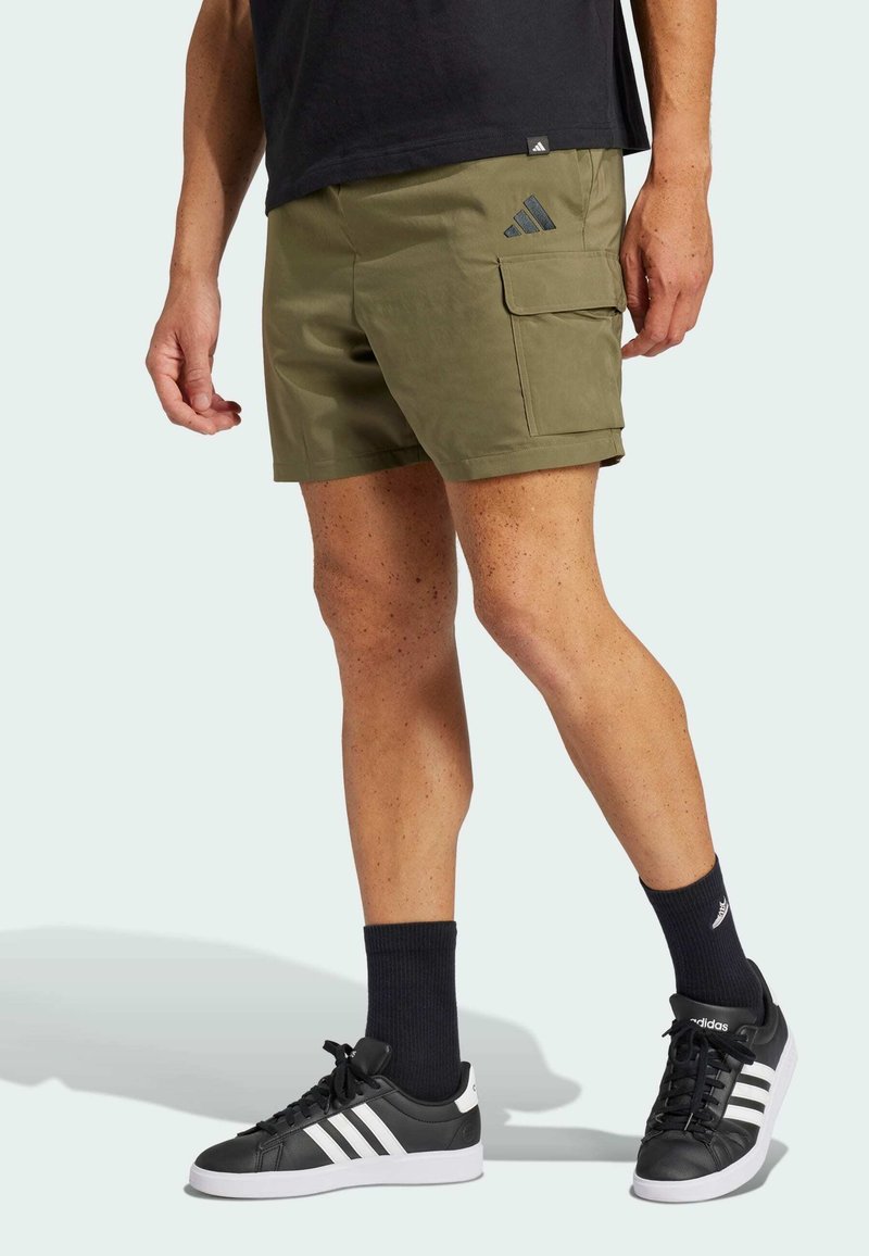 Olive green shorts with a cargo pocket, made of lightweight material. Paired with black sneakers, white stripes, and black socks.