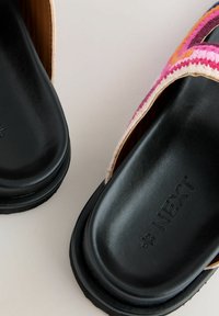 Sorte slidesandaler med en vævet multicolor rem og præget logo. Den teksturerede fodseng giver greb; den glatte overflade står i kontrast til remmen.