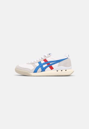 Baskets blanches à profil bas avec des accents en daim beige, des bandes latérales bleues et rouges, des lacets blancs et une semelle couleur crème.