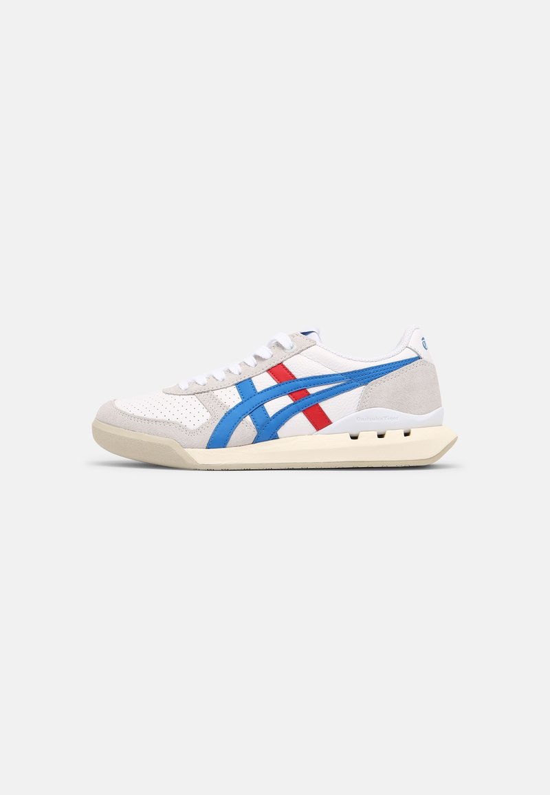 Baskets blanches à profil bas avec des accents en daim beige, des bandes latérales bleues et rouges, des lacets blancs et une semelle couleur crème.