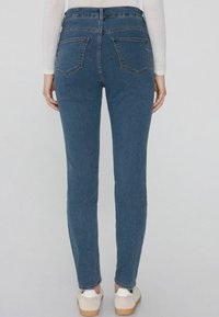 Modré džínové kalhoty s úzkým střihem, se dvěma zadními kapsami a středním pasem. Tkanina vypadá měkce s mírným strečem.