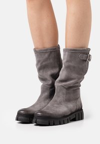 Botas de ante gris hasta la mitad de la pantorrilla con un diseño holgado, puntera redondeada y suela de goma negra con taco. Incluyen un adorno de hebilla lateral para estilo.