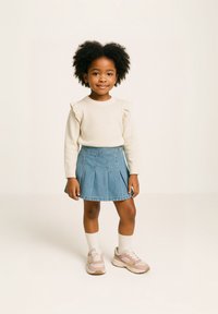 Ljus krämfärgad tröja med volanger på axlarna, ihop med en blå denimkjol. Vita strumpor och rosa sneakers med detaljer fulländar outfiten.