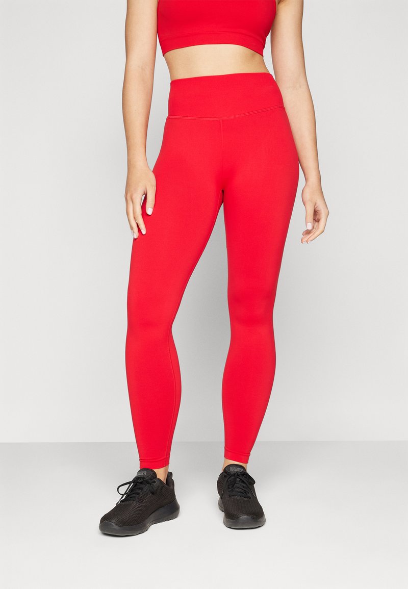 Røde høyt liv leggings laget av elastisk stoff med en glatt tekstur, kombinert med svarte treningsko.