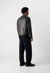Schwarze Lederjacke mit einer figurbetonten Passform, die eine glatte Oberfläche und feine Nähte aufweist. Kombiniert mit dunkelblauen weitgeschnittenen Jeans und schwarzen Schuhen.
