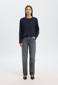 Dugi mornarski top s dugim rukavima, sive traperice ravnog kroja, crne cipele. Jednostavan dizajn, glatka tekstura i minimalna metalna oprema.