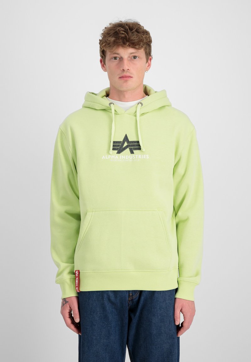 Sudadera verde claro con cordones y bolsillo frontal. Presenta una impresión de logo en negro. Combinada con vaqueros azules. Textura suave.
