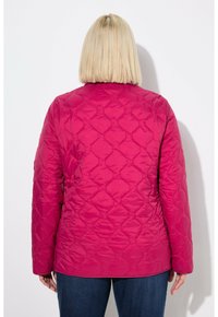 Chaqueta acolchada fucsia con cuello redondo y mangas largas. Presenta un patrón geométrico y una textura suave. Lleva puesta sobre unos jeans de mezclilla.