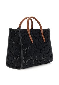 Bolso negro con textura de encaje floral y asas de cuero marrón, forma rectangular estructurada, vista en ángulo sobre fondo blanco.