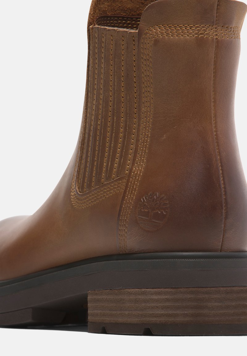 Bruine leren enkelboot met een gladde afwerking, elastische zijpanelen en een gestructureerde houten hak. Logo in de zijkant gegraveerd.
