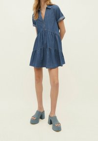 Denim jurk met korte omgeslagen mouwen, gelaagd ontwerp en v-hals. Gecombineerd met platform mules in zachtblauwe stof.
