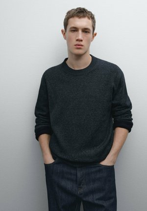 Pull gris foncé à col rond, avec des poignets côtelés et une texture douce, associé à un jean en denim foncé. Design simple sans motifs.