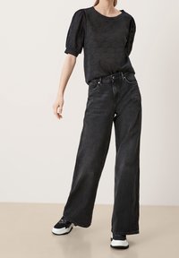 Sort tekstureret kortærmet top med rund hals, parret med højtaljede, vide sorte jeans og sort-hvide sneakers.