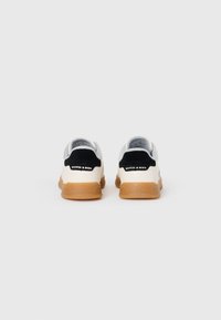 Sneakers with a gray suede and white textured upper, black heel accent, and gum rubber sole, featuring a logo on the back panel.
