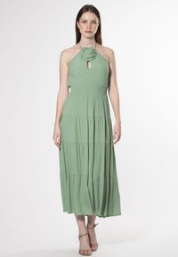 Vestido verde sin mangas con escote anudado y detalle de ojal, diseño en capas, textura suave y silueta hasta el tobillo.