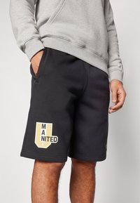 Černé bavlněné šortky s elastickým pasem, na levém stehně se nachází velké logo v žluté a bílé, které zní "MANITED".