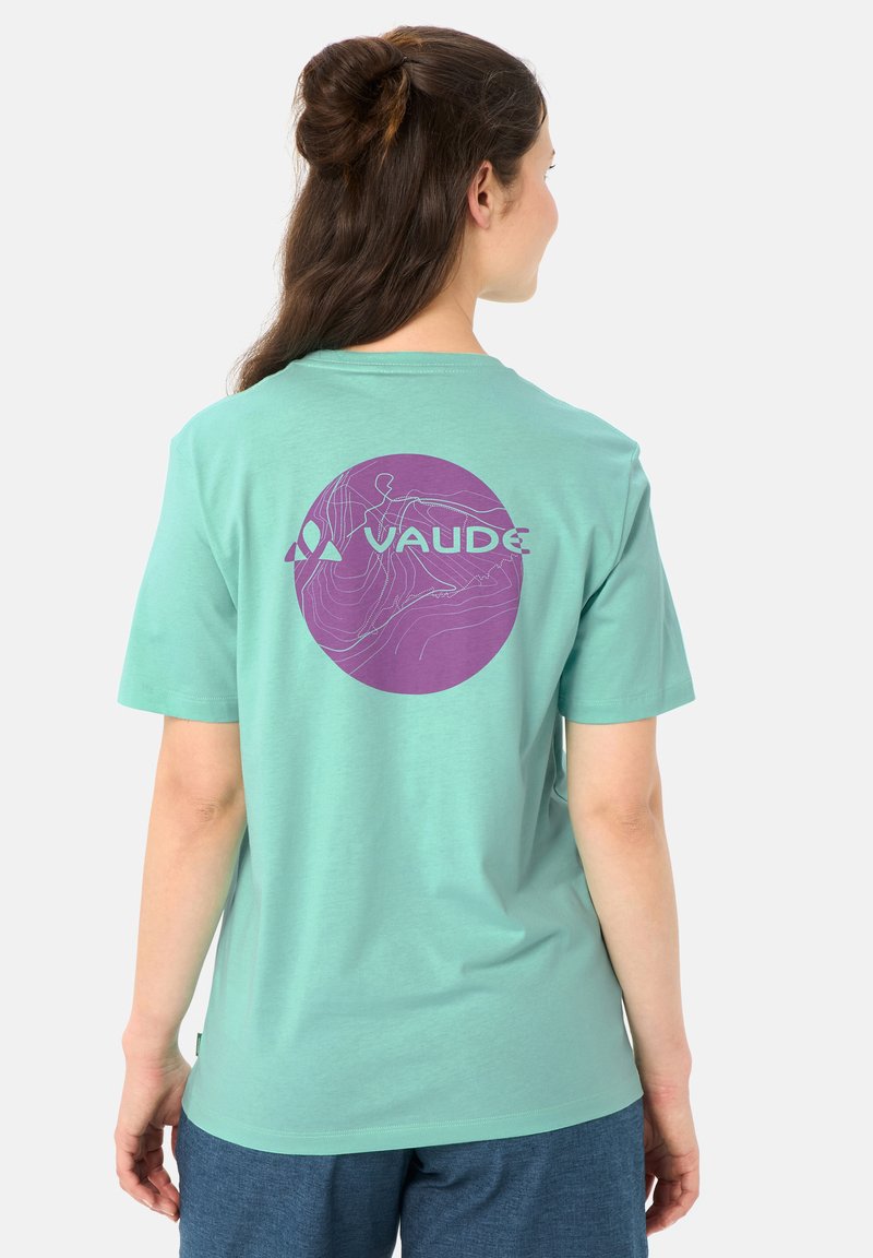 Femme vue de dos portant un T-shirt vert menthe avec un motif topographique circulaire violet et le logo "VAUDE", associé à un short bleu.