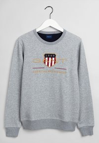 Felpa grigia con collo rotondo, con logo a scudo in rosso e giallo, con testo ricamato "GANT" e "AMERICAN SPORTSWEAR."