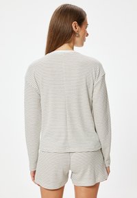 Stribet loungewear sæt i lys beige med mørke striber, der omfatter en langærmet top og shorts, lavet af blødt, tekstureret stof.