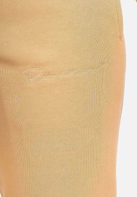 Lichtgele, zachte gebreide broek met een geborduurd logo in cursieve stijl aan de linkerkant, met een getailleerde pasvorm.