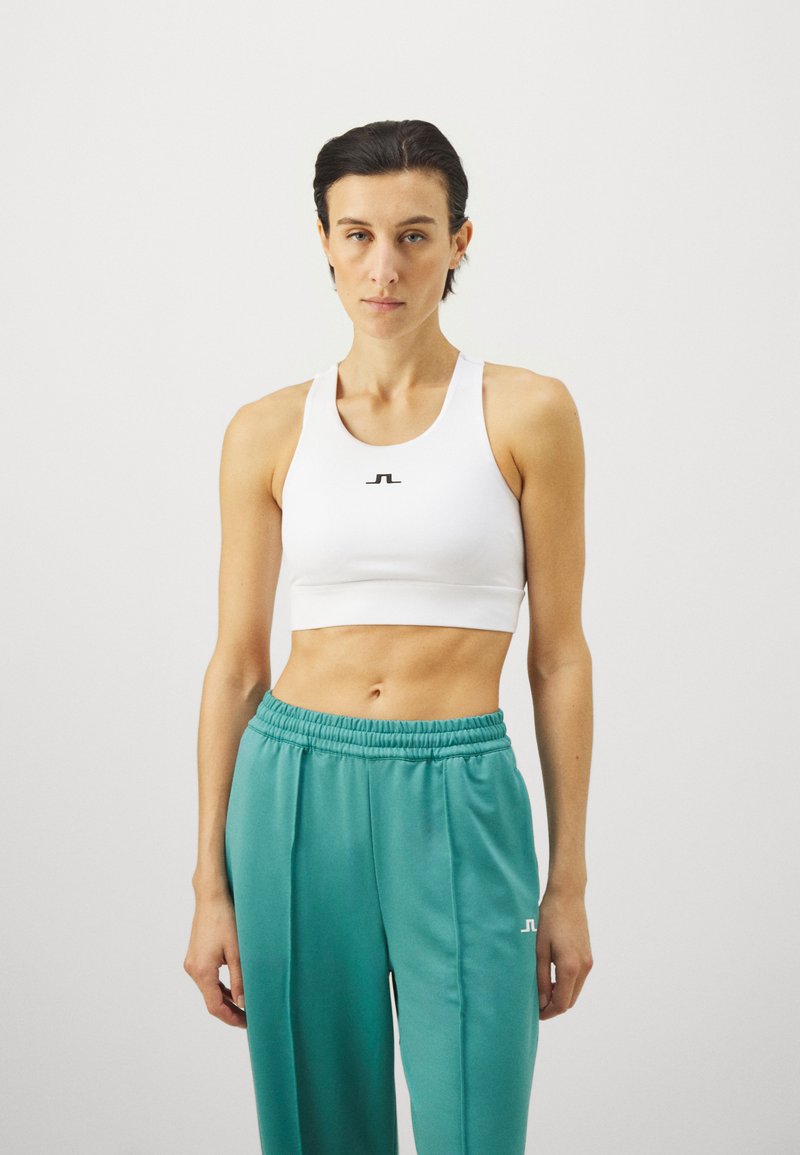 Λευκό αθλητικό σουτιέν με μαύρο λογότυπο, συνδυασμένο με γκρι βελουτέ παντελόνια με κορδόνι, που διαθέτουν μαλακό ύφασμα και άνετη εφαρμογή.